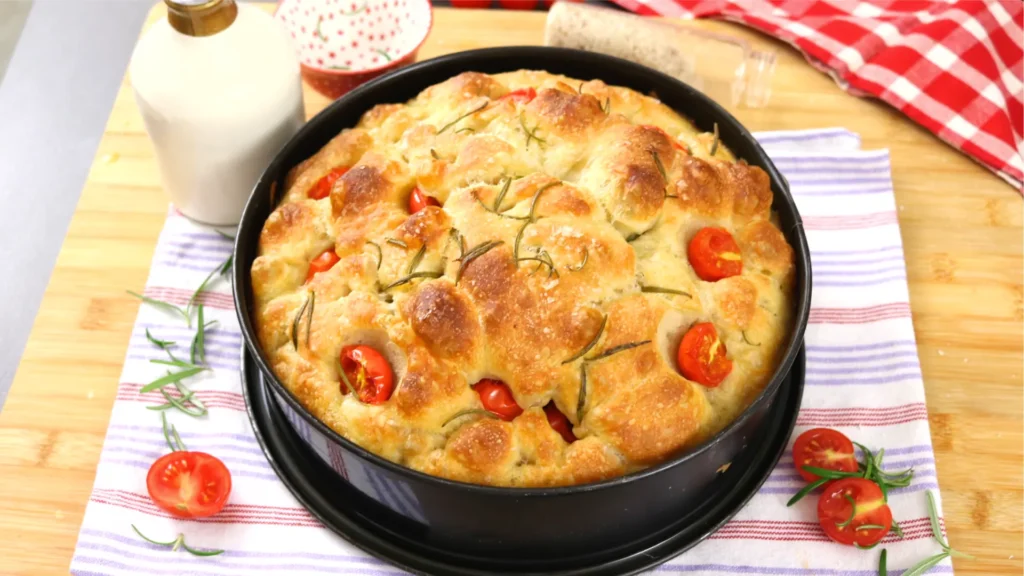 Focaccia sin amasar alta y esponjosa con tomates cherry y romero, horneada en molde redondo