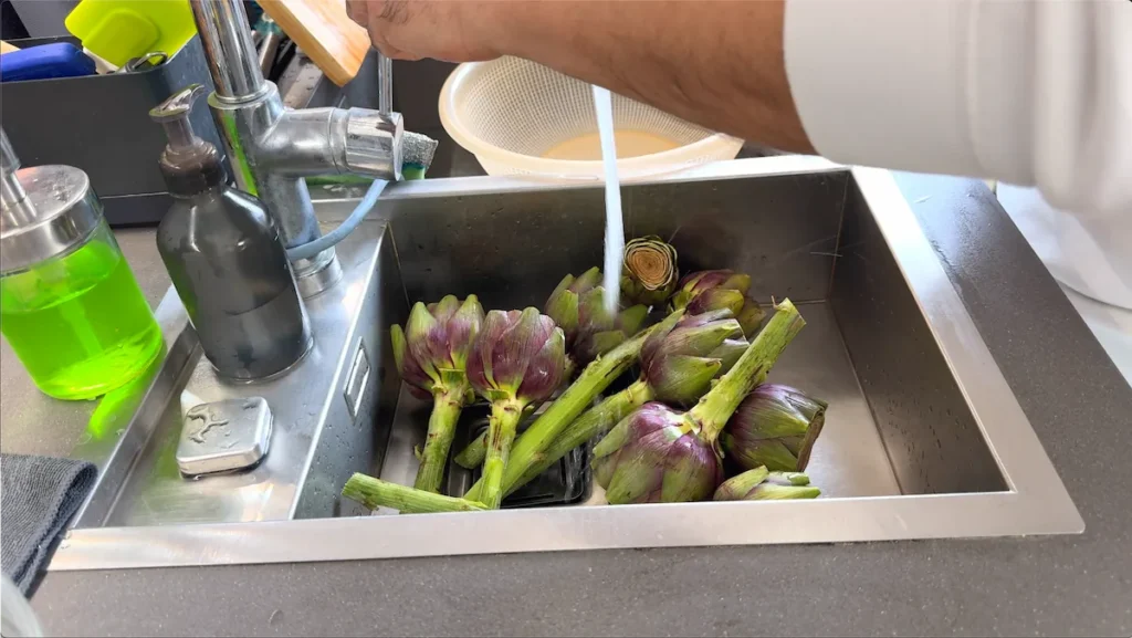 Alcachofas frescas siendo lavadas bajo el grifo con agua corriente para eliminar restos de tierra antes de su preparación